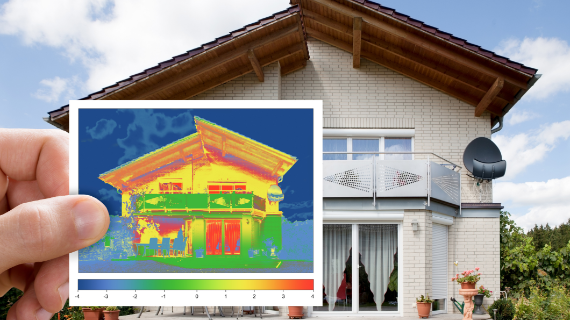 Eine Person hält ein Wärmebild eines Hauses vor dem tatsächlichen Haus, das die Temperaturverteilung auf der Fassade zeigt.