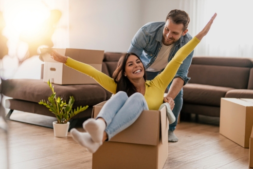 Drei Personen stehen in einem Wohnzimmer mit Umzugskartons und halten einen Schlüssel in den Händen.